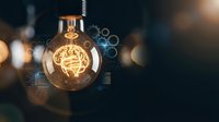 Glowing light bulb with brain filament surrounded by digital interface elements and bokeh lights representing innovation and creative thinking concepts.