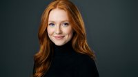 Professional redhead woman in black turtleneck smiling confidently against dark background for business portraits and corporate headshots.