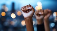 Raised fists of African American protesters against blurred city lights background, symbolizing unity, strength and social justice movement at dusk.
