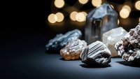 Assorted raw gemstones and crystals arranged on dark surface with warm bokeh lights creating luxurious jewelry making and mineral collection atmosphere.