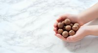 Hands holding macadamia nuts on marble surface. Suitable for food, nutrition, healthy eating, and culinary content.