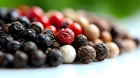 Colorful mix of whole peppercorns including black, white, pink, and red varieties arranged in diagonal line on white surface with soft focus background.