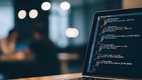 Software developer programming code on laptop screen in modern office environment with bokeh lights creating professional workspace atmosphere.