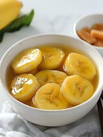 Sweet banana slices in golden syrup served in white bowl, traditional Asian dessert with honey glaze for healthy snacking and comfort food recipes.