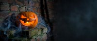 Carved jack-o-lantern with glowing face and blue smoke effect on weathered brick wall, creating spooky atmosphere for seasonal decorations and holiday celebrations.