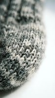 Close-up of a gray knitted wool hat with soft texture and intricate stitch detail, captured with shallow depth of field on a white background.
