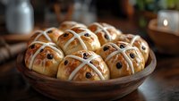 Fresh hot cross buns with raisins and white icing crosses arranged in wooden bowl on rustic table, traditional Easter holiday baking with golden crust.