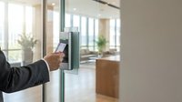 Professional businessman using modern electronic access control system with smartphone at glass office door for secure building entry and workplace security.