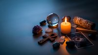 Mystical fortune telling setup with crystal ball, burning candle, tarot cards and spiritual objects on dark surface for divination practices.