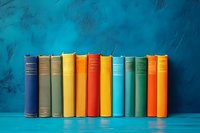 Row of colorful vintage hardcover books standing on turquoise wooden shelf against textured blue wall background, arranged by rainbow spectrum colors.