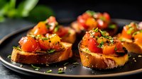 Toasted bread slices topped with fresh cherry tomatoes, herbs and seasonings on black plate, close up view with selective focus. Appetizing bruschetta.