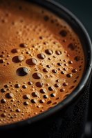 Fresh brewed coffee with rich crema and bubbles in black cup, close-up view for cafe menu, beverage advertising and morning drink concepts.