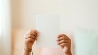 Hands holding blank white card against soft blurred background with warm natural light, suitable for mockups, presentations, and promotional designs.