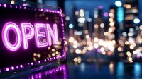 Bright neon open sign glowing in pink and purple lights against blurred city nightlife background with bokeh effects for business and retail concepts.