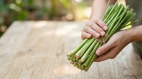 Fresh green asparagus bunch held in hands over wooden surface, suitable for cooking, nutrition, healthy eating, and farm-to-table food photography projects.