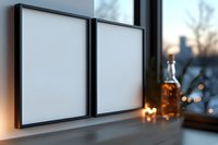 Two blank black frames on windowsill with whiskey bottle and blurred city lights background creating cozy evening atmosphere for home interior design.