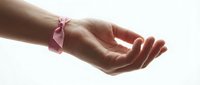 Female hands with pink ribbon tied around wrist in supportive gesture against clean white background for breast cancer awareness campaigns.