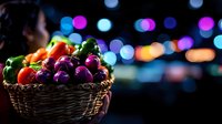 Fresh colorful bell peppers and tomatoes in wicker basket against blurred bokeh lights background, creating moody atmospheric food photography.