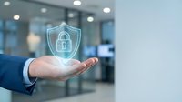 Businessman in blue suit holding glowing shield with padlock icon, representing data protection, cybersecurity, and digital safety in modern office environment.