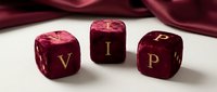 Three luxury burgundy dice with golden VIP letters on white surface with red silk fabric background for premium gaming and exclusive entertainment concepts.