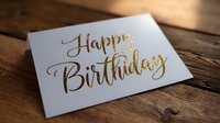 Gold glitter lettering Happy Birthday on white greeting card placed on rustic wooden table surface with natural lighting and shallow depth of field.