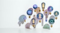 Collection of vintage Edison bulbs and LED lights with colorful cosmic galaxy designs casting shadows on white background for creative lighting projects.