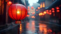 Traditional red paper lantern glowing on rainy evening street with blurred bokeh lights reflecting on wet pavement, creating atmospheric Asian ambiance.
