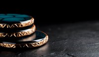 Stacked golden rings with ornate tribal pattern design on dark textured background with dramatic lighting and copy space for jewelry marketing and retail displays.