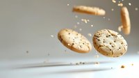 Crispy round crackers with sesame seeds falling and crumbling against neutral gray background, creating dynamic food composition.
