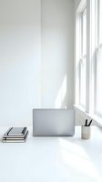 Minimalist white workspace with laptop, notebooks and pen holder by bright window. Clean modern home office setup with natural light for productivity and focus.