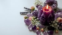Purple amethyst crystals arranged with lit candle, dried flowers and lavender sprigs for meditation, healing rituals and spiritual wellness practices.