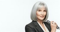 Mature woman with silver gray bob hairstyle and bangs, wearing black blazer, holding microphone, isolated on white background for corporate, broadcast, and professional use.