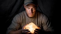 Caucasian male soldier in military uniform and cap holding glowing light cube in dark tent, representing hope, innovation, and futuristic technology in combat zone.