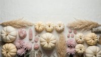 Autumn flat lay with cream pumpkins, pink mums, wheat stalks and decorative elements on neutral background for seasonal design projects.