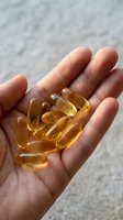 Close-up of hand holding golden amber gel capsules, supplements or vitamins. Ideal for health, wellness, nutrition and medical content.