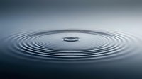 Water drop creating concentric ripples on calm surface, suitable for backgrounds, meditation, wellness, and abstract design projects.