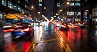 Blurred city street at night with colorful traffic lights and car headlights creating bokeh effect on wet pavement during evening rush hour in urban downtown area.