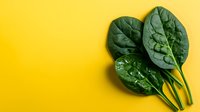 Fresh green spinach leaves on bright yellow background with copy space for healthy eating and nutrition concepts.