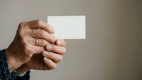 Mature male hand holding blank white business card against neutral background for corporate branding and marketing purposes.