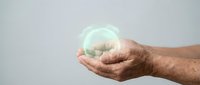 Male hands holding glowing green energy sphere with light effects against neutral background for environmental and sustainability concepts.