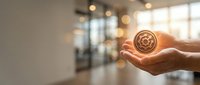 Hand holding golden cryptocurrency coin in modern office space with blurred background, representing digital finance and blockchain technology investment.