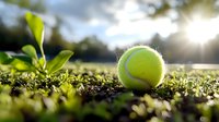 Bright yellow tennis ball resting on grass with sunlight flare, creating natural outdoor sports atmosphere for recreational activities.
