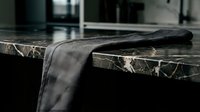 Folded gray linen fabric draped over dark marble countertop in modern kitchen setting, showcasing textile texture and interior design styling for home decor projects.