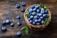 Fresh ripe blueberries in wicker basket with green leaves on rustic wooden background, scattered berries around, macro food photography.