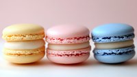 Three colorful French macarons in yellow, pink and blue arranged in row on soft pink background for bakery menu, dessert photography or culinary design.