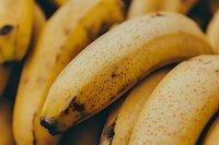 Ripe yellow bananas with natural brown spots on dark background, macro close-up view showing fresh fruit texture and natural aging pattern.