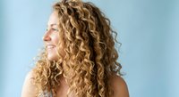Young Caucasian woman with long curly blonde hair smiling, side profile view against light blue background, natural beauty concept.