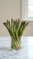 Fresh green asparagus spears in glass on marble counter in bright kitchen interior for healthy cooking and spring vegetable preparation.