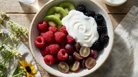 Healthy breakfast bowl with fresh berries, kiwi slices, grapes and yogurt on rustic wooden table for nutritious morning meal and wellness lifestyle.