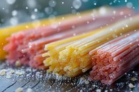 Colorful raw pasta spaghetti in yellow, pink and red colors arranged on rustic wooden surface with water drops and bokeh effect, perfect for Italian cuisine design.